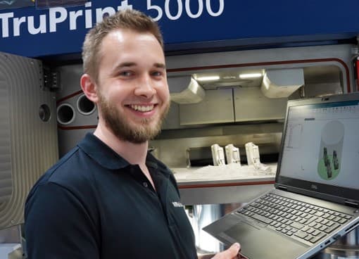 Kevin Epple vor einer TruPrint 5000 mit CAD-Daten auf Laptop | Kevin Epple in front of a TruPrint 5000 with CAD data on a laptop 