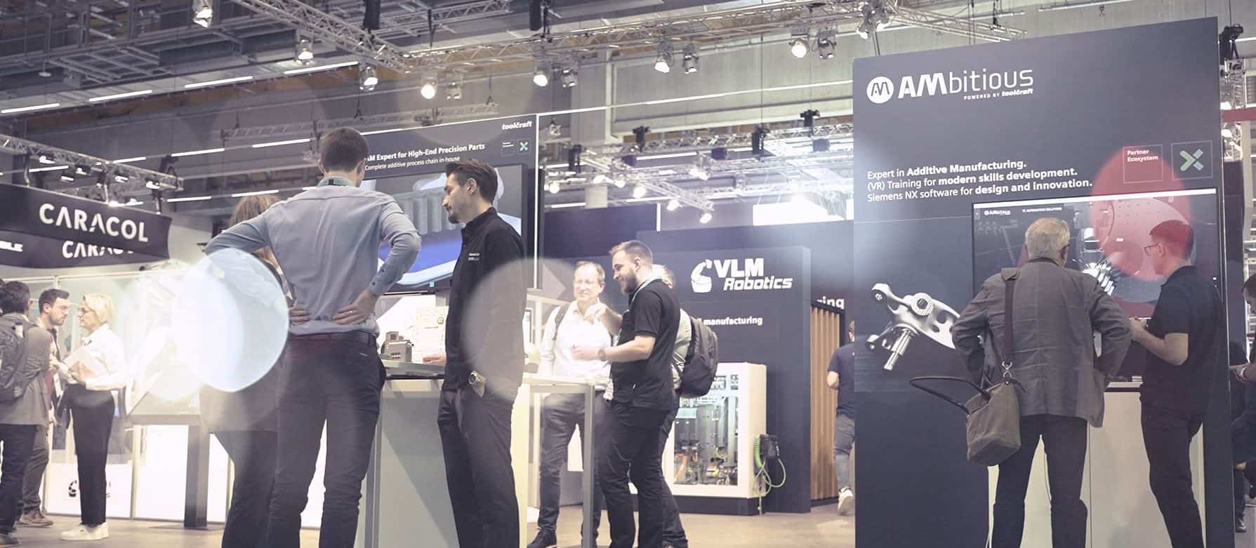 Messestand von AMbitious auf der Formnext 2024 mit mehreren Besuchern, Präsentation moderner Technologien für Additive Fertigung | Booth of AMbitious at Formnext 2024 with multiple visitors, showcasing modern technologies for Additive Manufacturing.